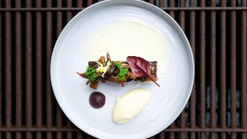 Une assiette blanche contenant un plat de viande, des légumes et une cuillerée de sauce, le tout posé sur une grille métallique.