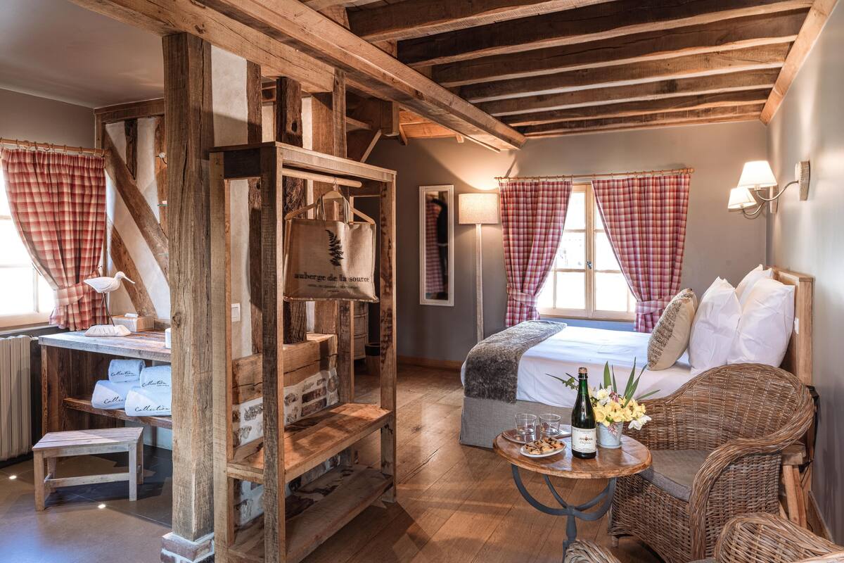 A rustic room with a wooden desk, a bed with checkered curtains, and wicker furniture.