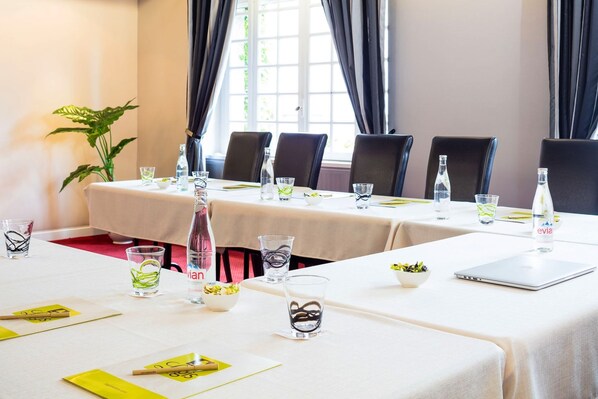 A conference room with tables set for a meeting, equipped with laptops, water bottles, and glasses.