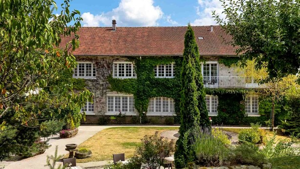 A two-story building with a red-tiled roof, ivy-covered walls, and a garden with outdoor seating.