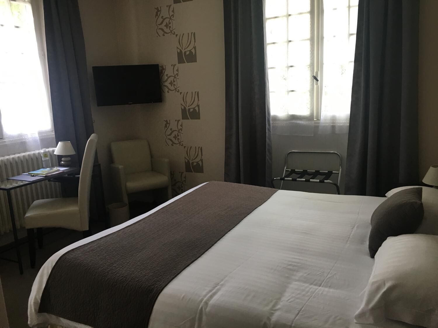 Habitación de hotel con cama, escritorio, silla, televisor y ventana con cortinas.