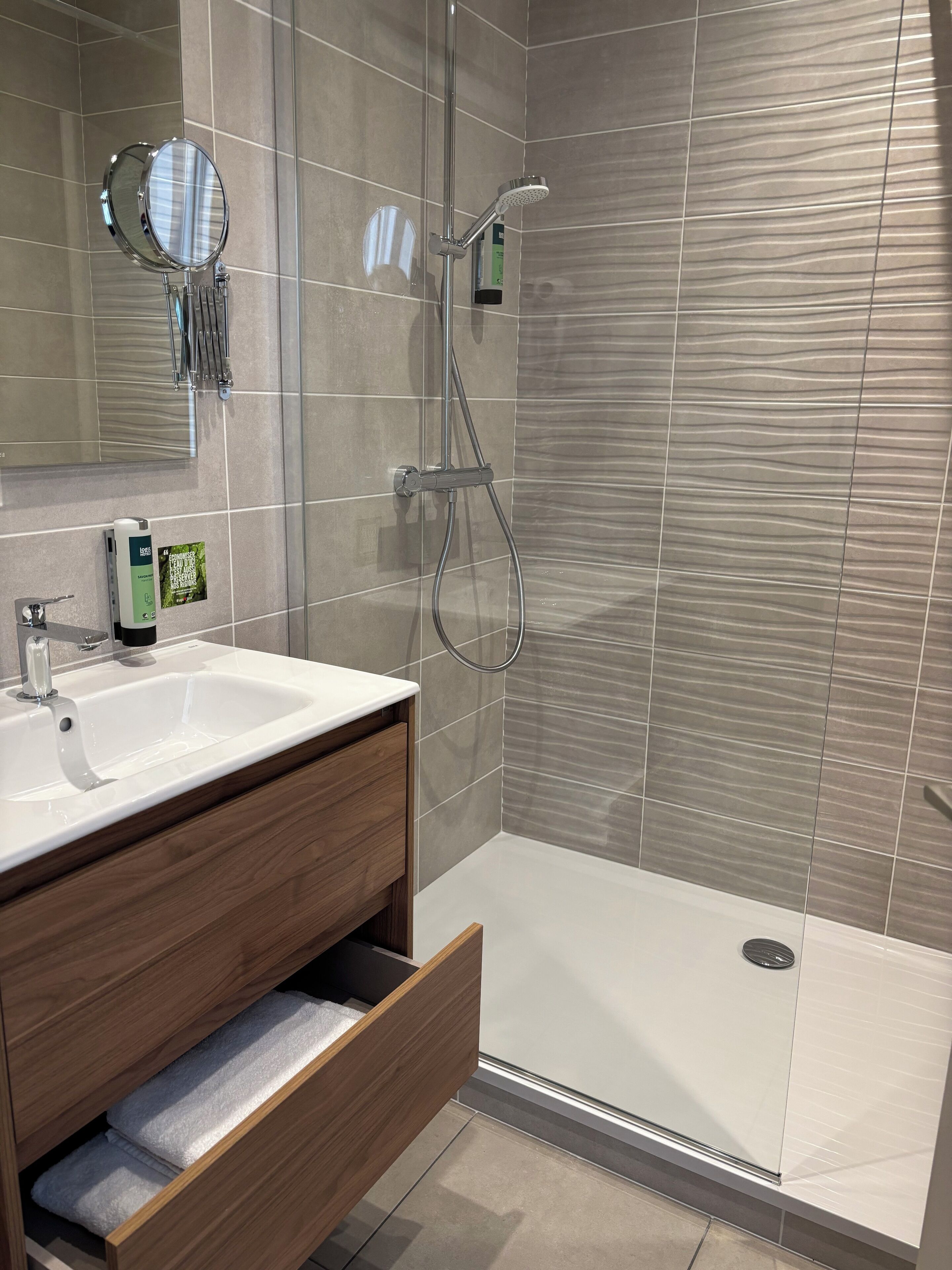 A modern bathroom with a white sink, wooden vanity, a mirror, and a shower area with a glass door.