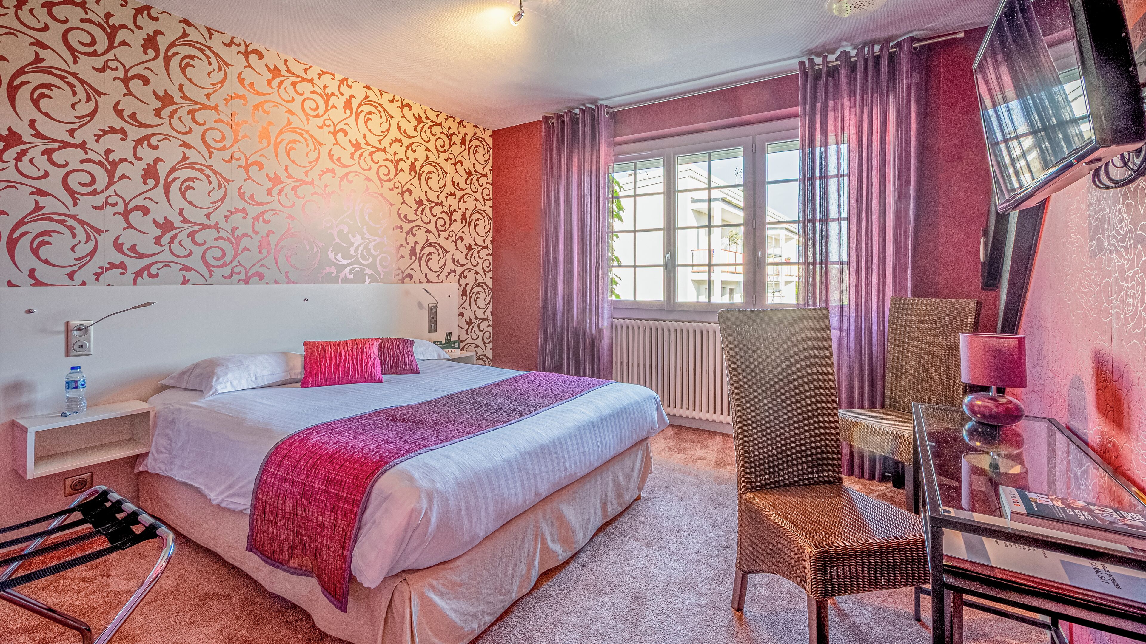 Habitación de hotel con cama, una silla, una mesa y ventana con cortinas.