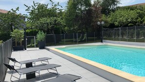 A swimming pool with a tiled deck, surrounded by a fence and trees.