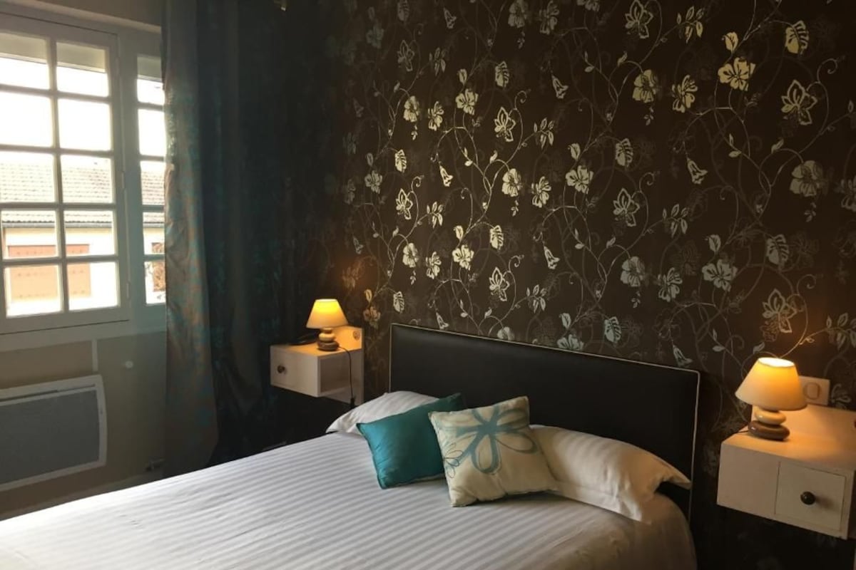 A hotel room with a bed, two bedside tables with lamps, a window with curtains, and a floral wallpaper.