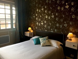 A neatly made bed with two pillows, a bedside table with a lamp, and a wall with floral wallpaper.