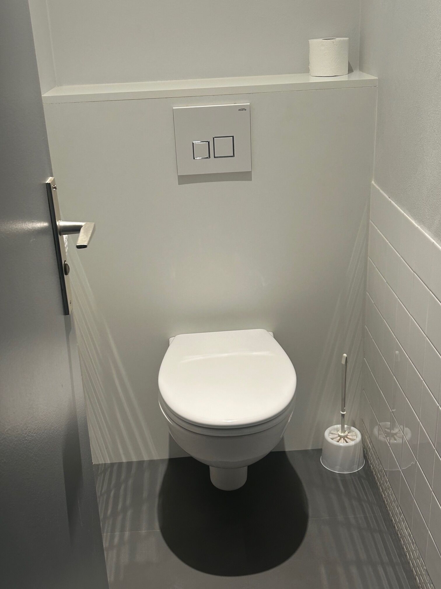 Un baño moderno con inodoro blanco, dispensador de papel higiénico y émbolo.