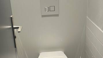 Un baño moderno con inodoro blanco, dispensador de papel higiénico y émbolo.