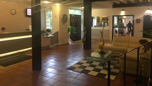 A hotel lobby with a reception desk, a checkered rug, a sofa, and a staircase.