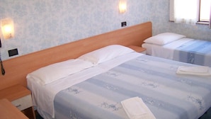 Une chambre d’hôtel avec un grand lit, un lit plus petit, une table de chevet, un téléphone et deux lampes fixées au mur.