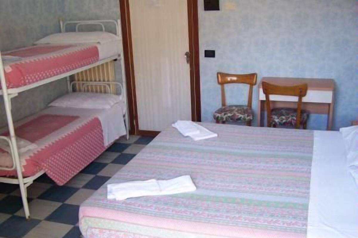 Een kamer met stapelbedden, een enkel bed, een stoel en een klein tafeltje.