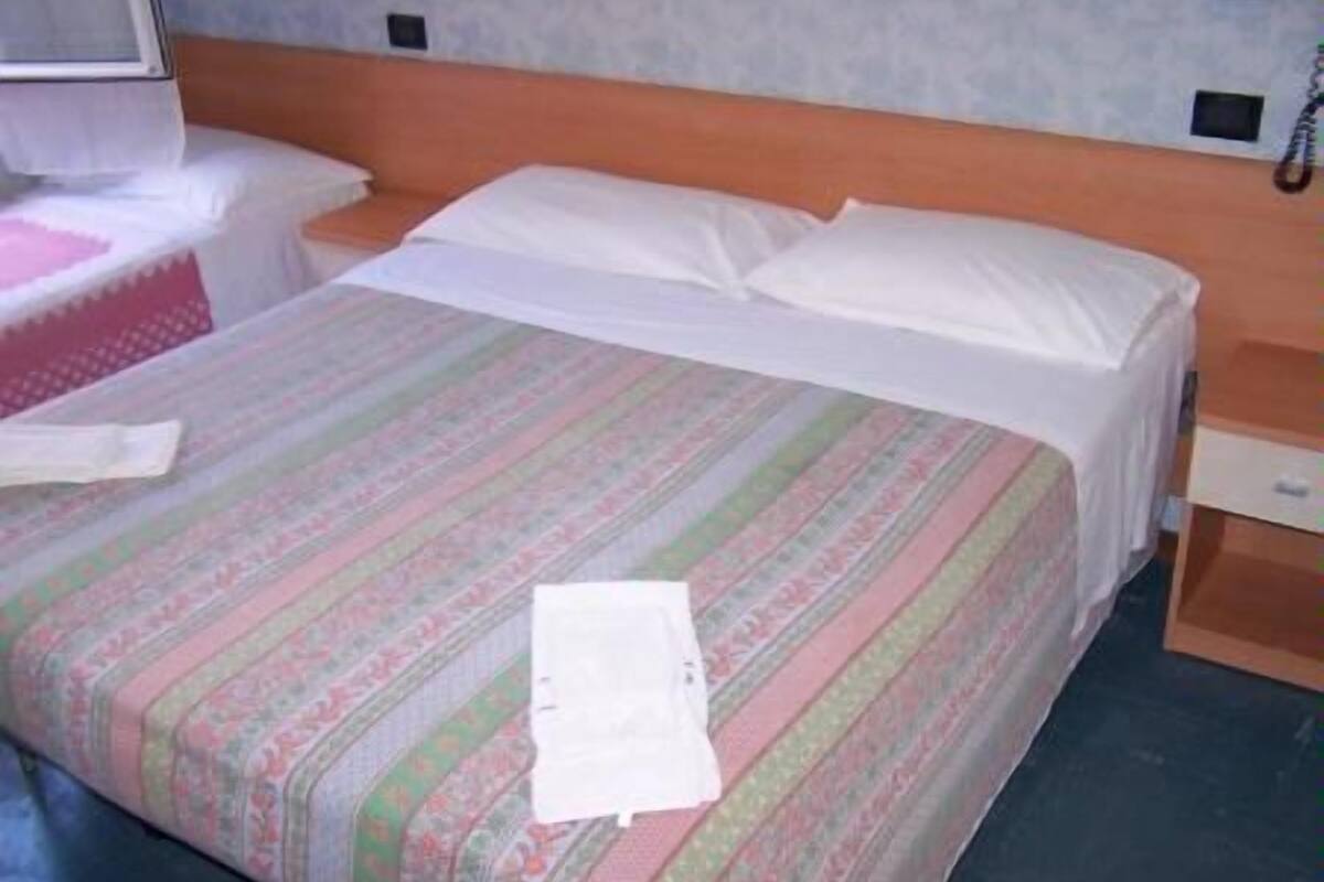 Een bed met een gestreept dekbedovertrek, een wit kussen en een witte deken.