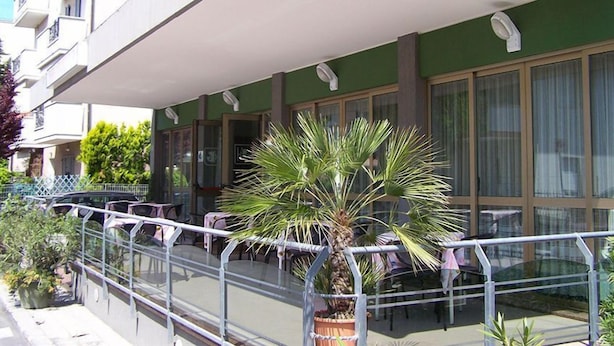 Un hôtel doté d’un espace extérieur couvert avec des sièges, d’un palmier et d’une rambarde.