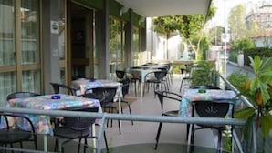 Un café en plein air avec des tables et des chaises, un espace de repos couvert et une vue sur la rue.