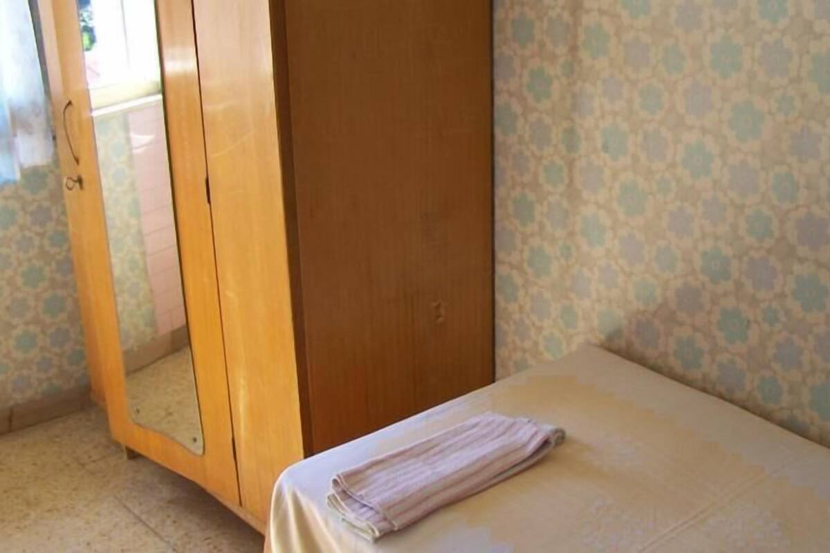 Een kamer met een bed, een houten garderobe en een behang met patroon.