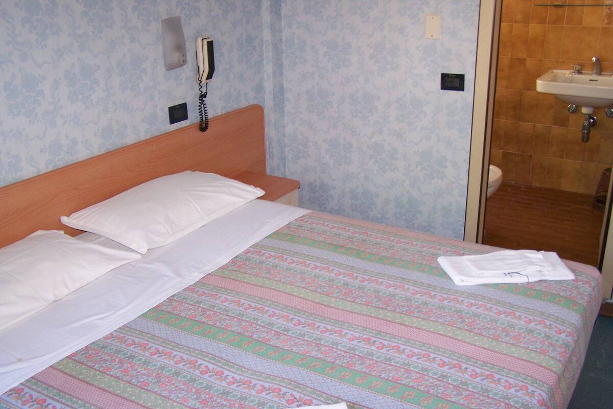 Een hotelkamer met een bed, een bedtafeltelefoon en een badkamer met een wastafel.