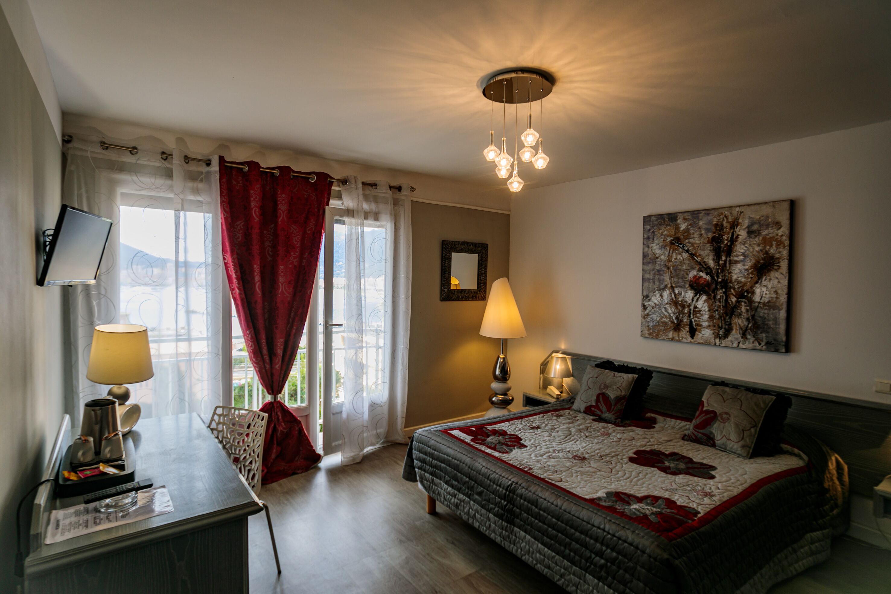 A hotel room with a bed, a desk with a lamp, a TV, and a window with curtains.