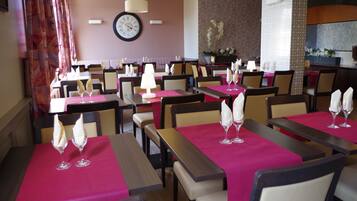 A restaurant with multiple tables, each with a pink tablecloth and a wine glass.