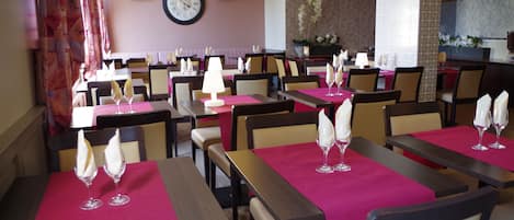 Restaurante com várias mesas, cada uma com toalha de mesa rosa e um copo de vinho.
