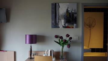 Ein Zimmer mit einem Tisch, einer violetten Lampe, einer Blumenvase und zwei Kunstwerken an der Wand.