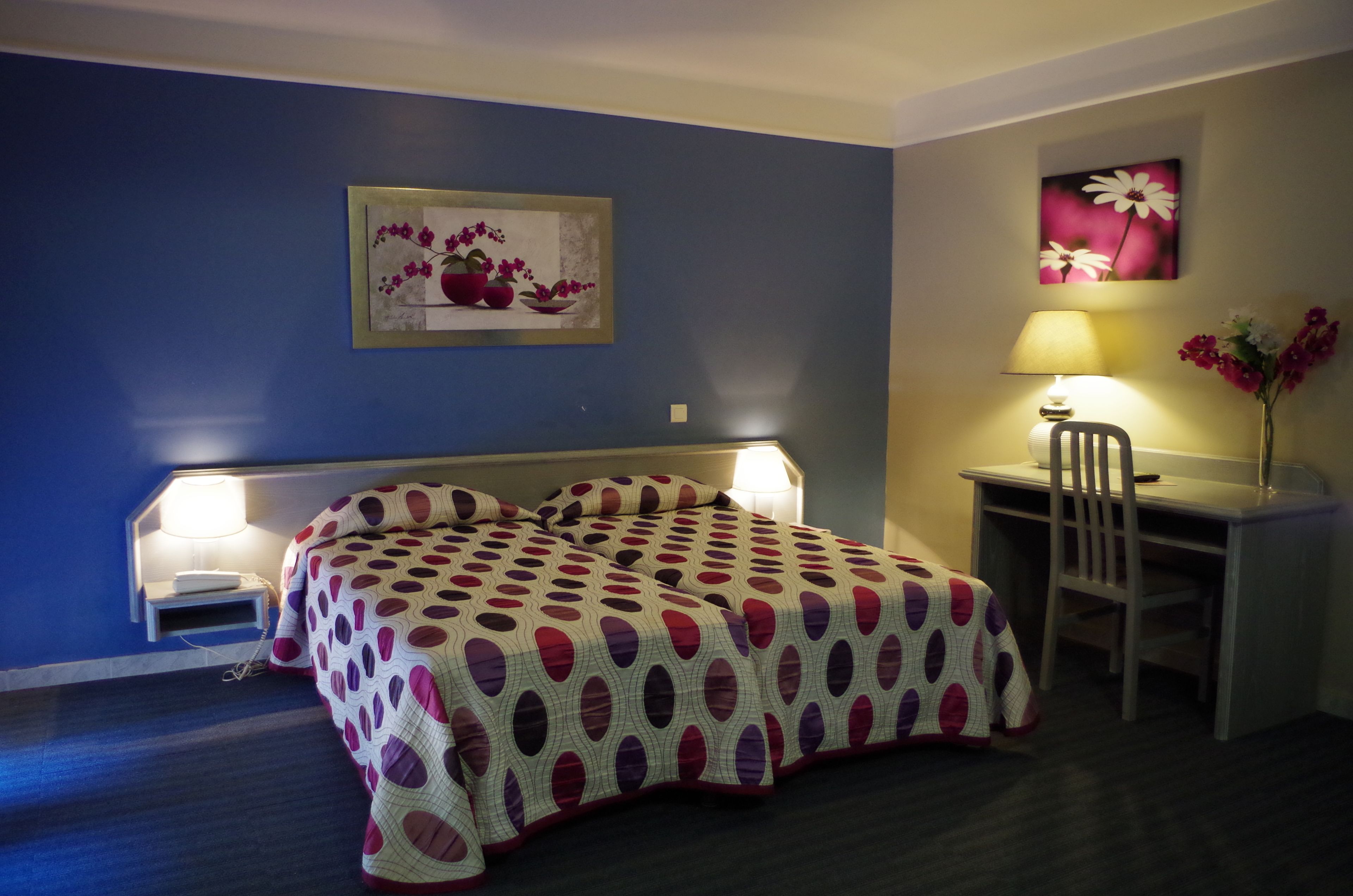 Un dormitorio con una cama, un escritorio, una silla y dos lámparas fijadas a la pared.