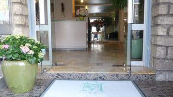 Entrada de hotel con suelo de mármol, una planta en maceta verde y un felpudo con el nombre del hotel.