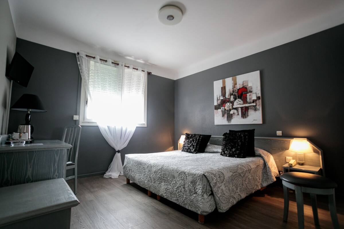 Ein Schlafzimmer mit Bett, Nachttisch, Lampe, Sessel und einem Bild an der Wand.