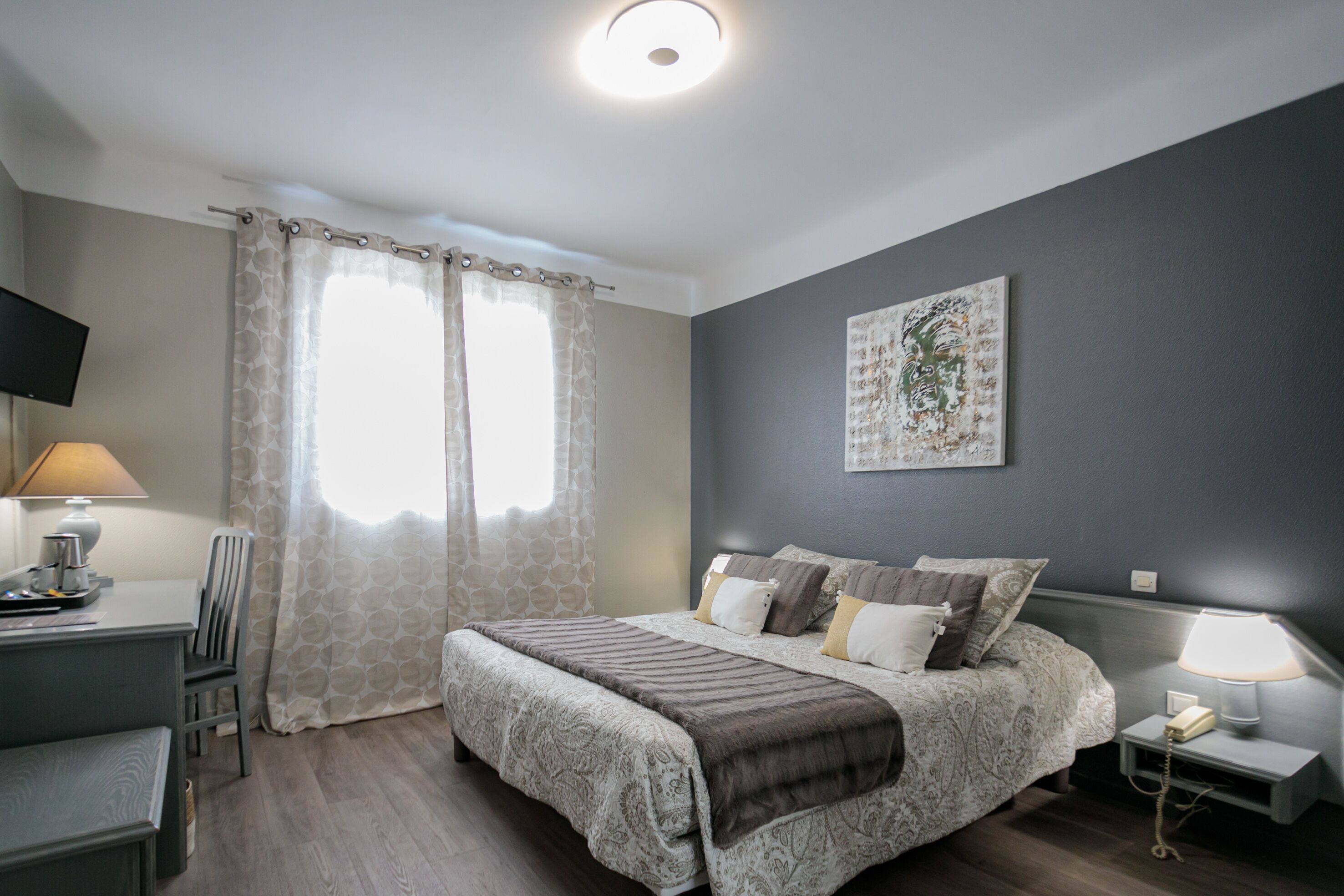 Un dormitorio con cama, mesita de noche, lámpara y televisor sobre un soporte.