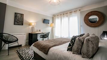 A bedroom with a bed, a desk, a chair, a TV, and a large mirror.