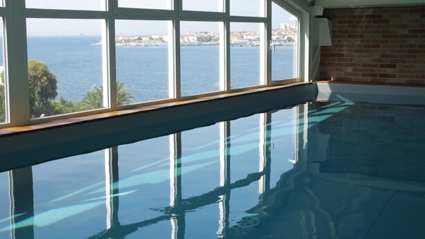 An indoor swimming pool with a view of the sea and buildings through large windows. - Spunta Di Mare (Ajaccio)