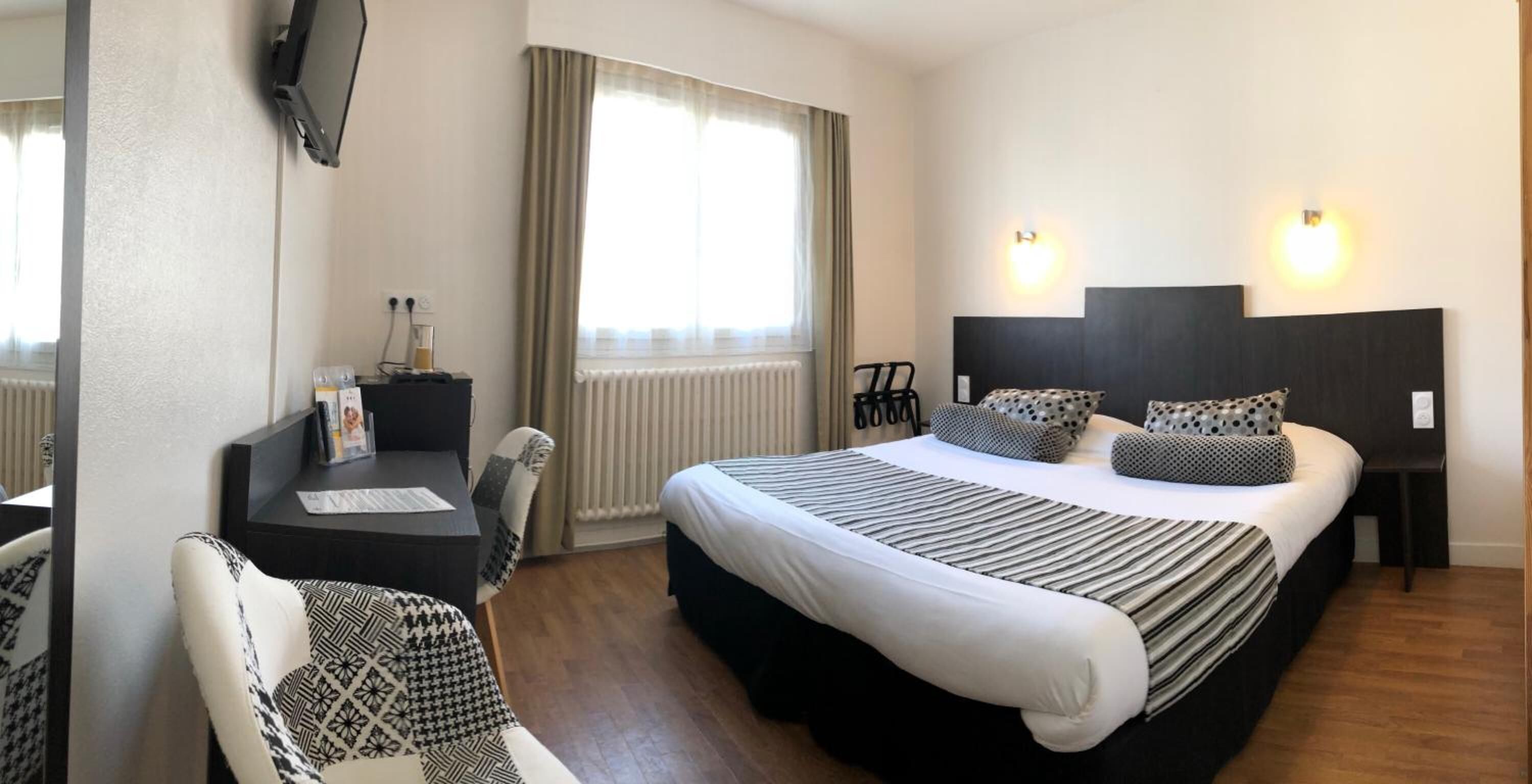 A hotel room with a bed, a desk, a chair, and a TV mounted on the wall.