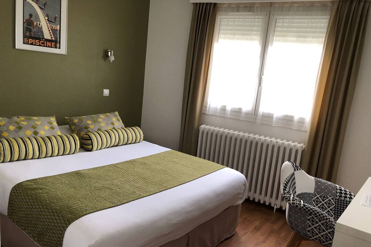 Una habitación de hotel con cama, radiador, ventana con cortinas y un cartel en la pared.