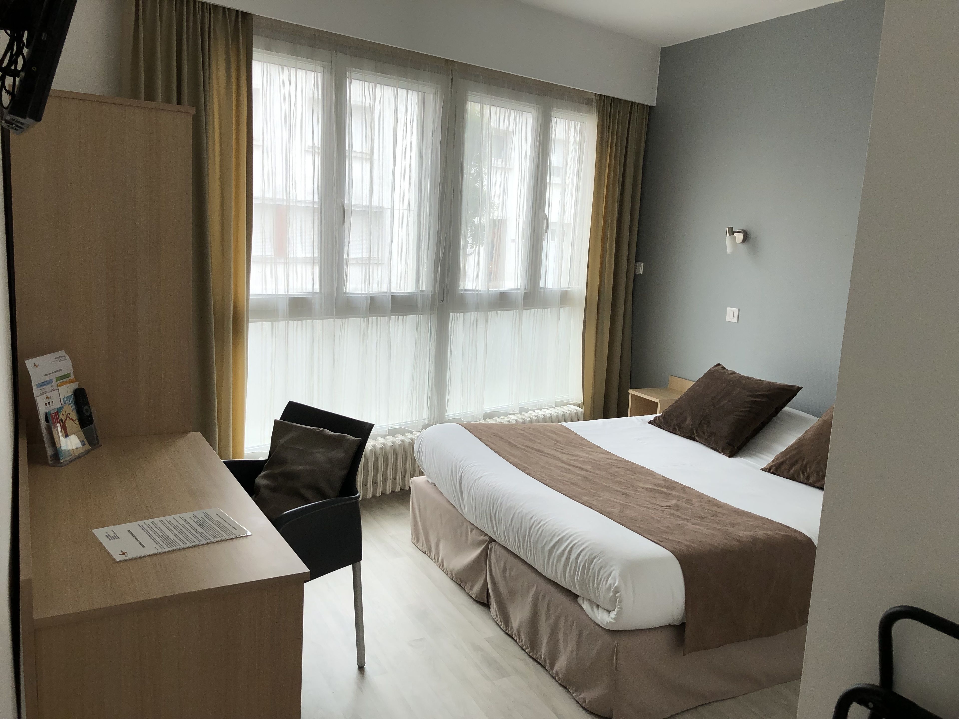 Une chambre d’hôtel avec un lit, un bureau, une chaise et une fenêtre avec des rideaux.