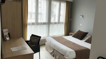 Une chambre d’hôtel avec un lit, un bureau, une chaise et une fenêtre avec des rideaux.