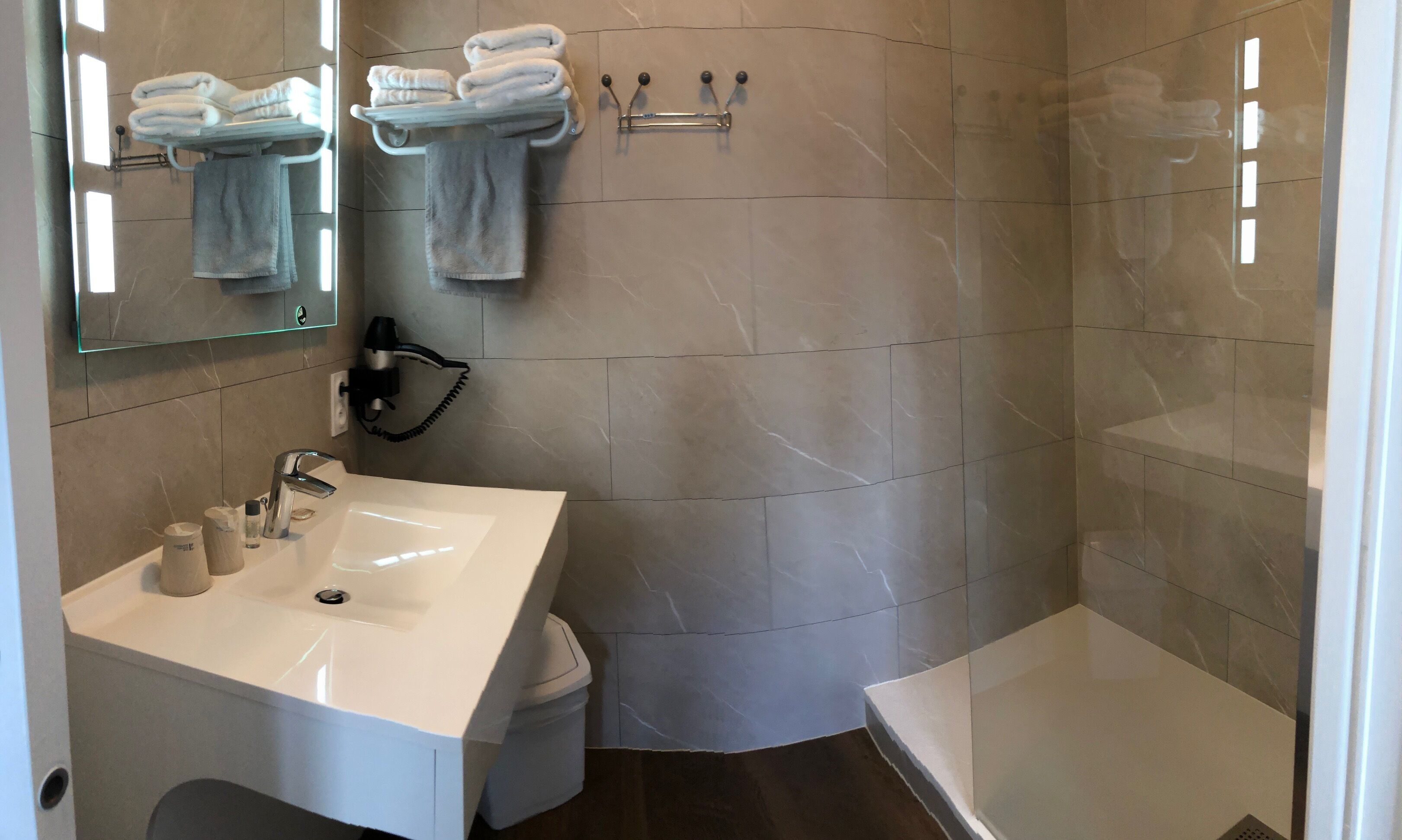 Un baño moderno con un lavamanos blanco, un espejo, un perchero con toallas dobladas y una zona de ducha.