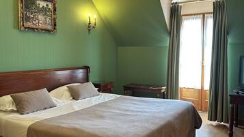 A large bed with a wooden headboard, a chandelier, a framed picture on the wall, and a window with curtains.
