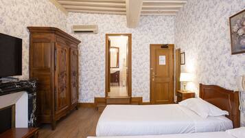 A hotel room with two beds, a wooden wardrobe, a television, a desk, and a bathroom visible through an open door.