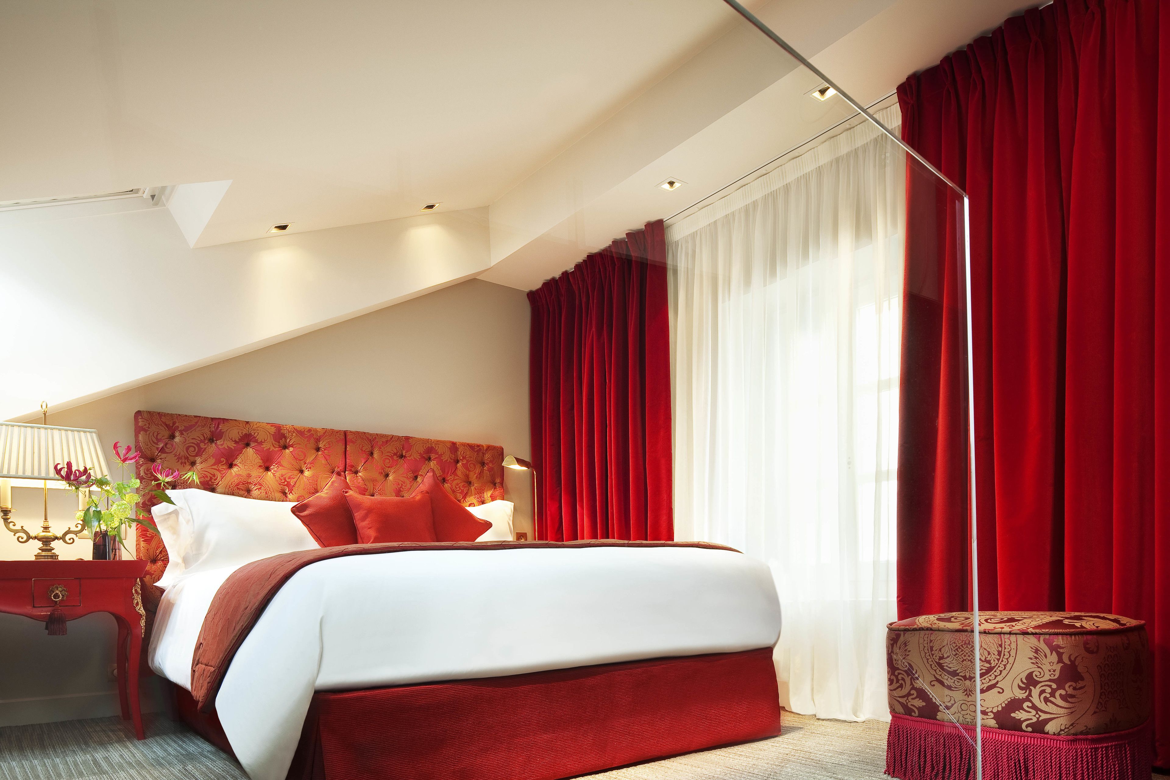 A hotel room with a large bed, red curtains, and a patterned ottoman.