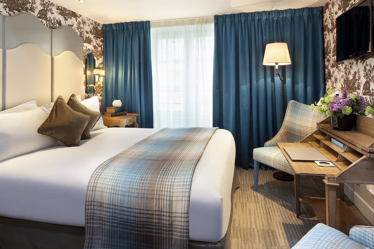 A hotel room with a large bed, a desk, a chair, a lamp, and a TV.