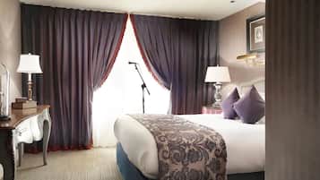A hotel room with a bed, two bedside lamps, a desk with a lamp, a microphone stand, and a framed picture on the wall.