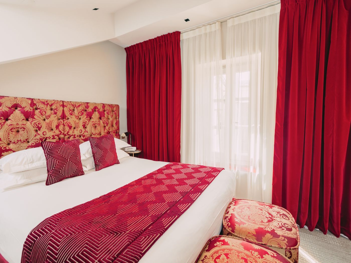 A hotel room with a large bed, red curtains, and a patterned headboard.
