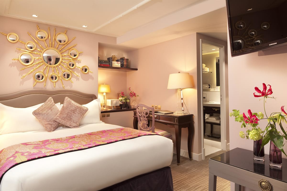 A hotel room with a large bed, a desk, a chair, a TV, and a decorative mirror on the wall.