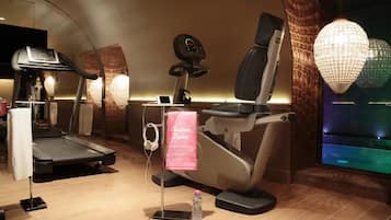 Espaço fitness com esteira, elíptica e bicicleta ergométrica, uma garrafa de água e um porta-toalhas.