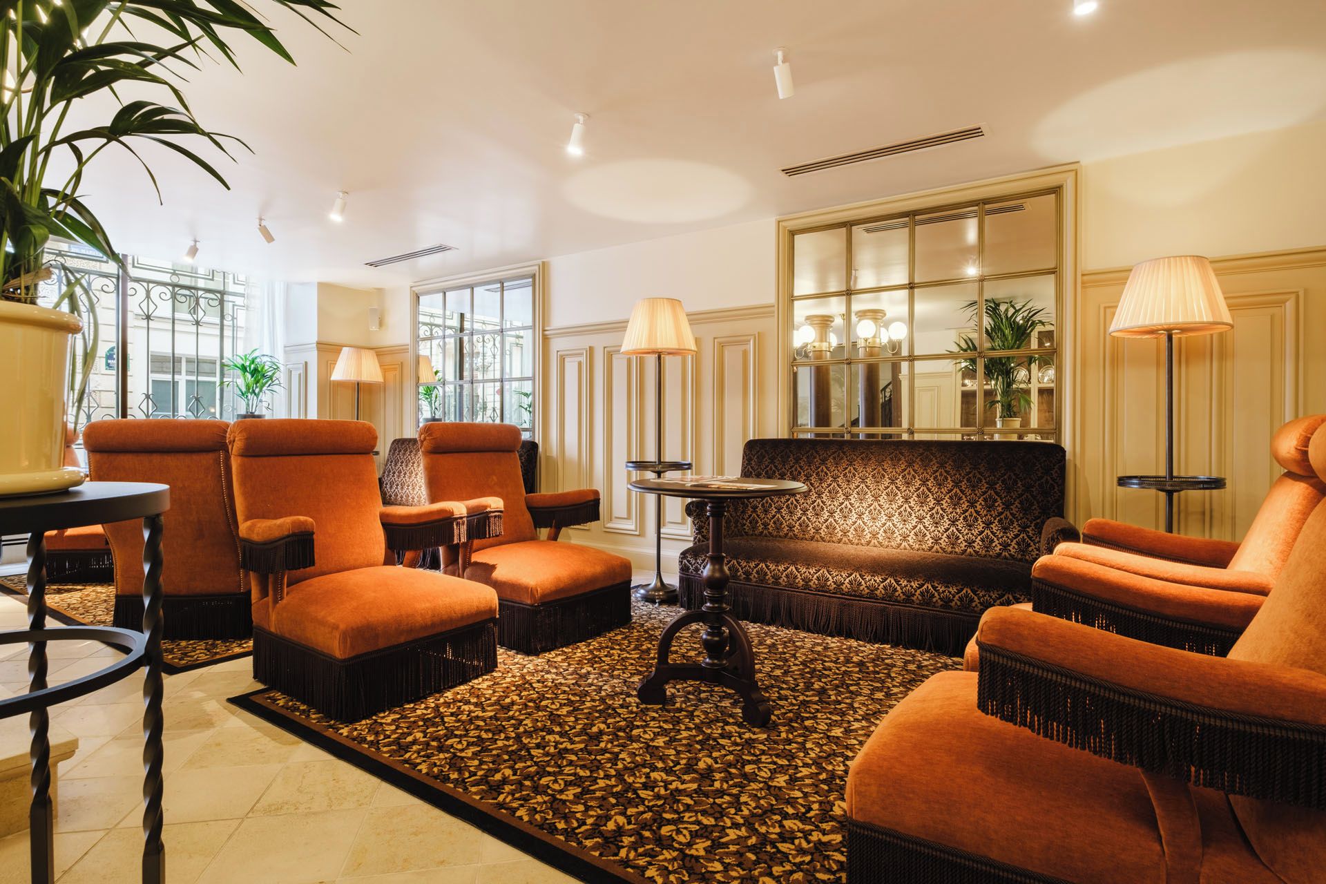 A room with a patterned sofa, armchairs, and a small table, with a decorative rug and a potted plant.