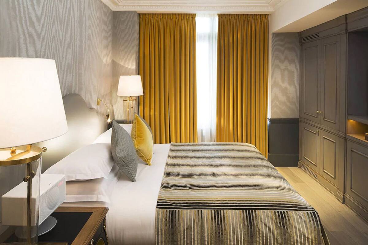 A hotel room with a large bed, two bedside tables with lamps, a wardrobe, and a view of the outside through curtains.