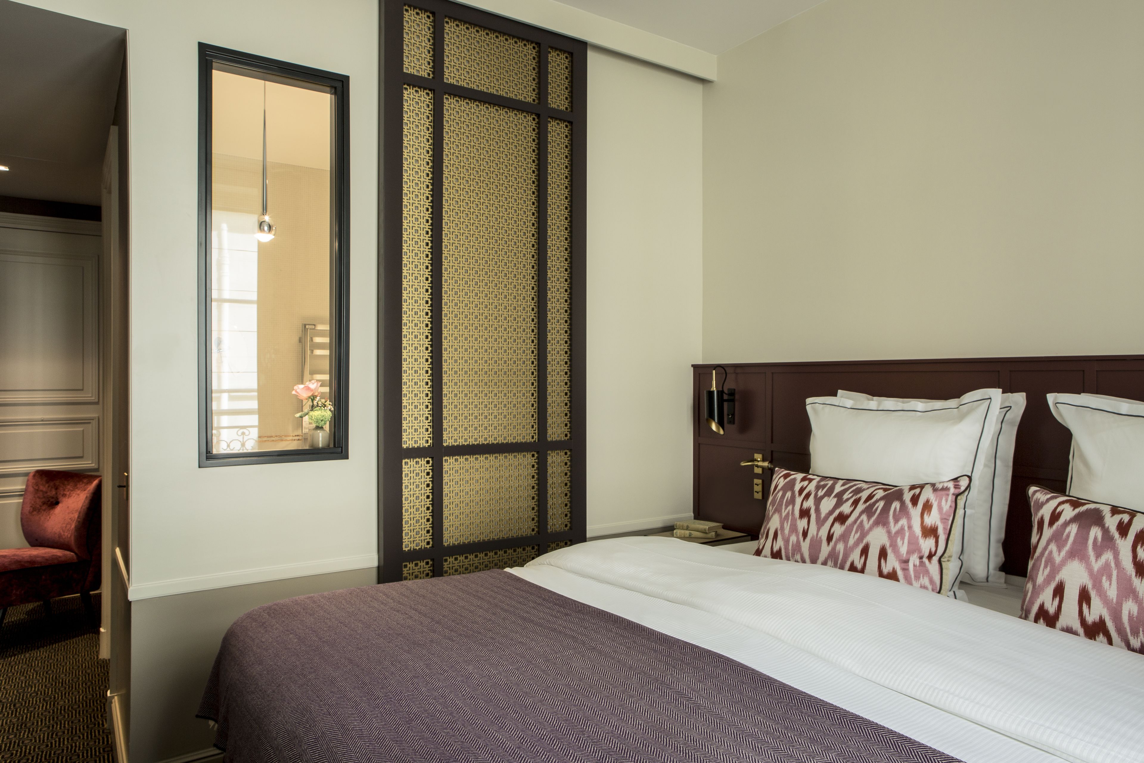 Una habitación de hotel con una cama grande, un armario, una silla y un biombo decorativo.