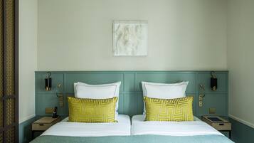 Un lit double avec des oreillers à motifs blancs et jaunes, une tête de lit de couleur turquoise et une petite table de chevet avec une lampe et un livre.