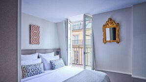 Una camera d'albergo con un letto, un'ampia finestra, uno specchio e un'opera d'arte appesa al muro.