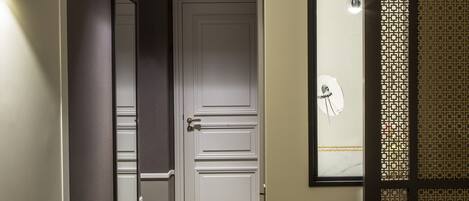 A hotel room with a bed, a desk with a lamp, a mirror, and a door leading to another room.