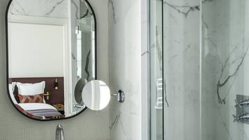 A modern bathroom with a marble sink, a large mirror, and a glass-enclosed shower.